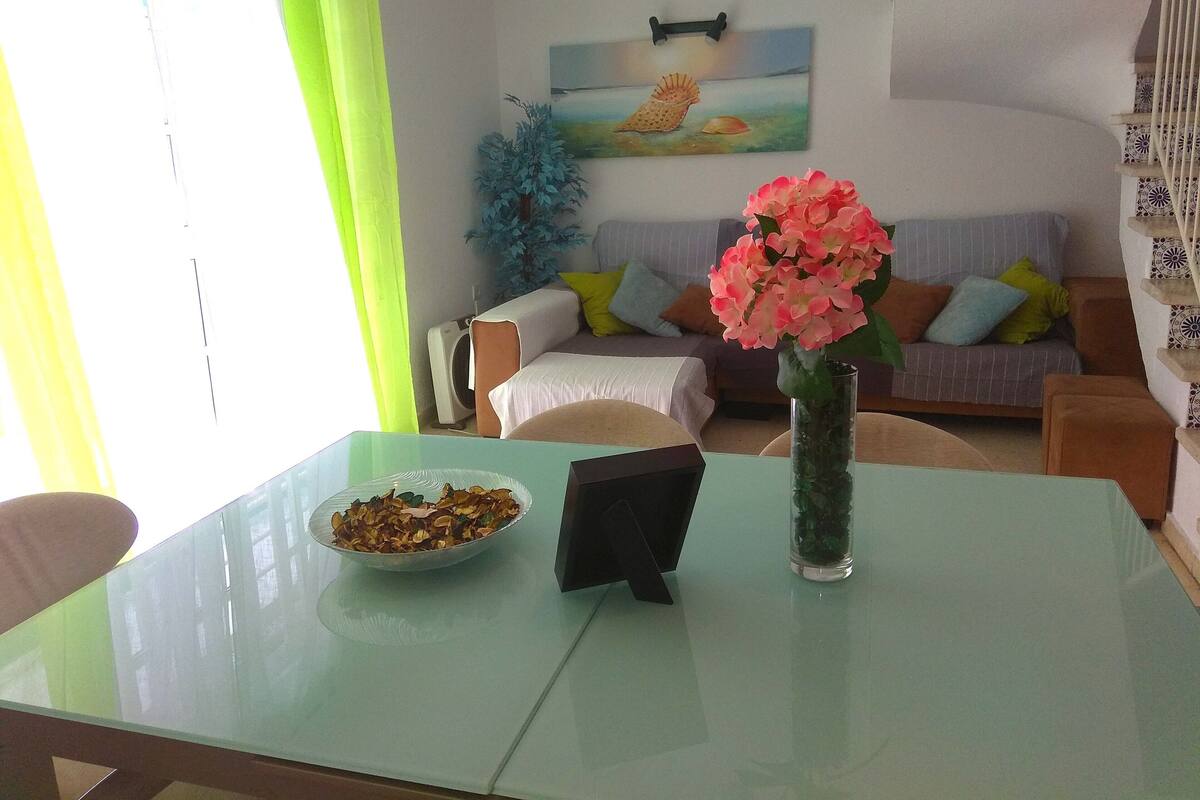 Ein Essbereich mit einem Glastisch, einer Schüssel mit Snacks und einer Vase mit Blumen.