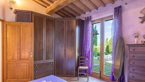 A bedroom with a large wardrobe, a bed with a purple bedspread, a chair, a dresser, and a window with purple curtains. - lovely ground floor cottage, sleeps 6 set in a tranquil ,private and panoramic position – completely (MONTICIANO)