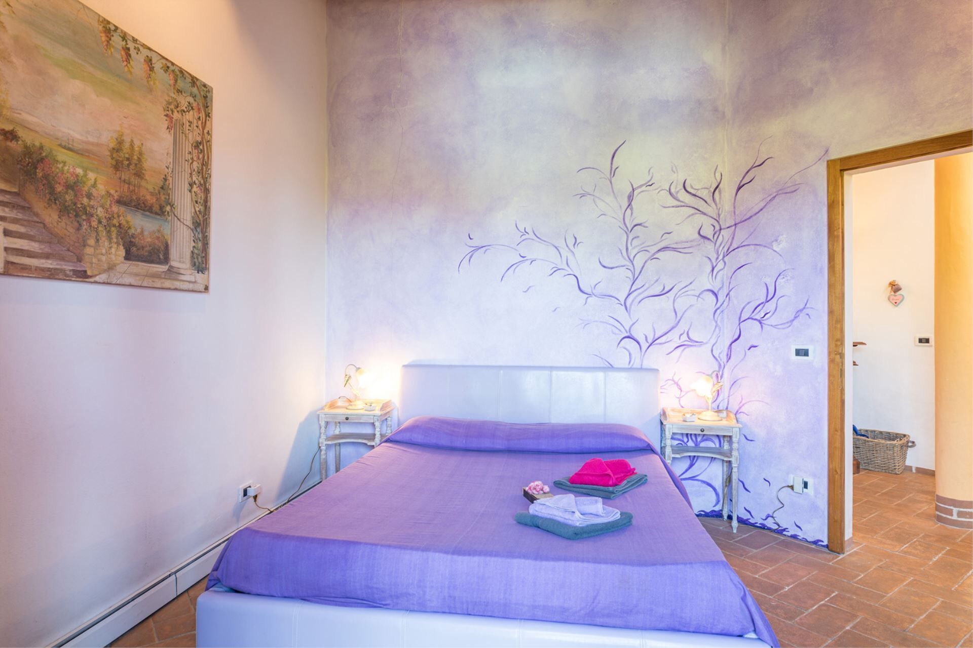 Una camera da letto con un letto, due comodini, un affresco sulla parete e una porta.