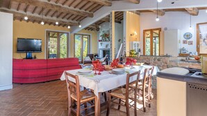 A dining area with a table set for four, wooden chairs, a red sofa, and a television in the background. - lovely ground floor cottage, sleeps 6 set in a tranquil ,private and panoramic position – completely (MONTICIANO)