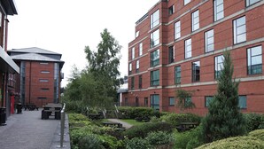 A courtyard with benches, a pathway, and a building with red brick walls and multiple windows. - Broad Gauge Apartments (Wolverhampton)
