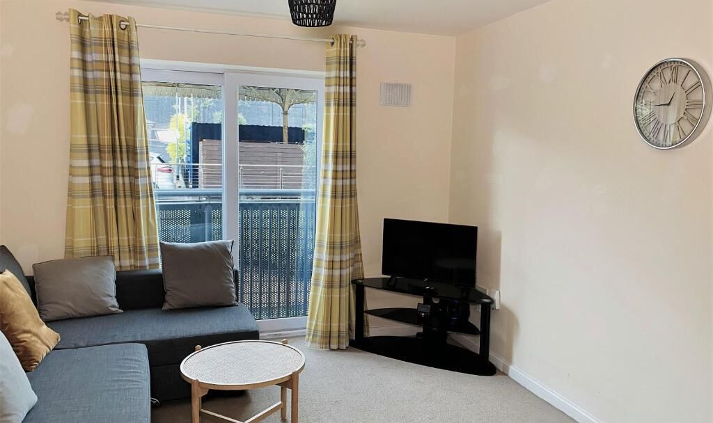 A living room with a sofa, a small round table, a TV on a stand, and a window with curtains.