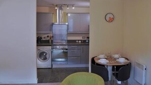 A compact kitchen with a washing machine, a stove, and a dining area with a table set for four. - Broad Gauge Apartments (Wolverhampton)