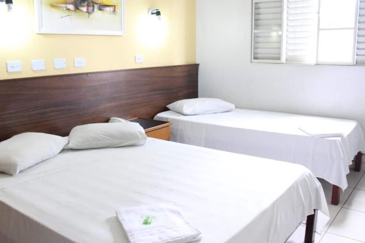 A hotel room with two single beds, a wooden headboard, a wall-mounted light fixture, and a window with shutters.