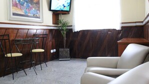 A living room with a beige sofa, a small table with two chairs, a TV mounted on the wall, and a potted plant. - Hotel Bell Vale (São José dos Campos)