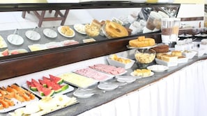 Een buffet met diverse etenswaren, zoals fruit, gebak en vlees.