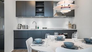 Eine moderne Küche mit dunklen Schränken, einem weißen Esstisch, der mit blauen Schüsseln und Weingläsern gedeckt ist, und einer Pendelleuchte darüber.