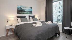 Ein modernes Hotelzimmer mit einem großen Bett, einem Nachttisch mit Lampe, einem Fenster mit Vorhängen und Blick auf die Stadt.