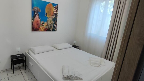 Ein Schlafzimmer mit einem Bett, einem Nachttisch, einem Gemälde und einem Fenster mit Vorhängen.
