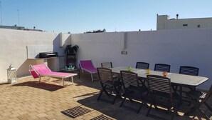Eine Terrasse mit Tisch, Stühlen, einem Grill und einer Liege.