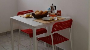 Ein Essbereich mit einem weißen Tisch und roten Stühlen, einem Brotkorb, einer Kaffeemaschine und einem Teller mit Brot und einer Tasse.