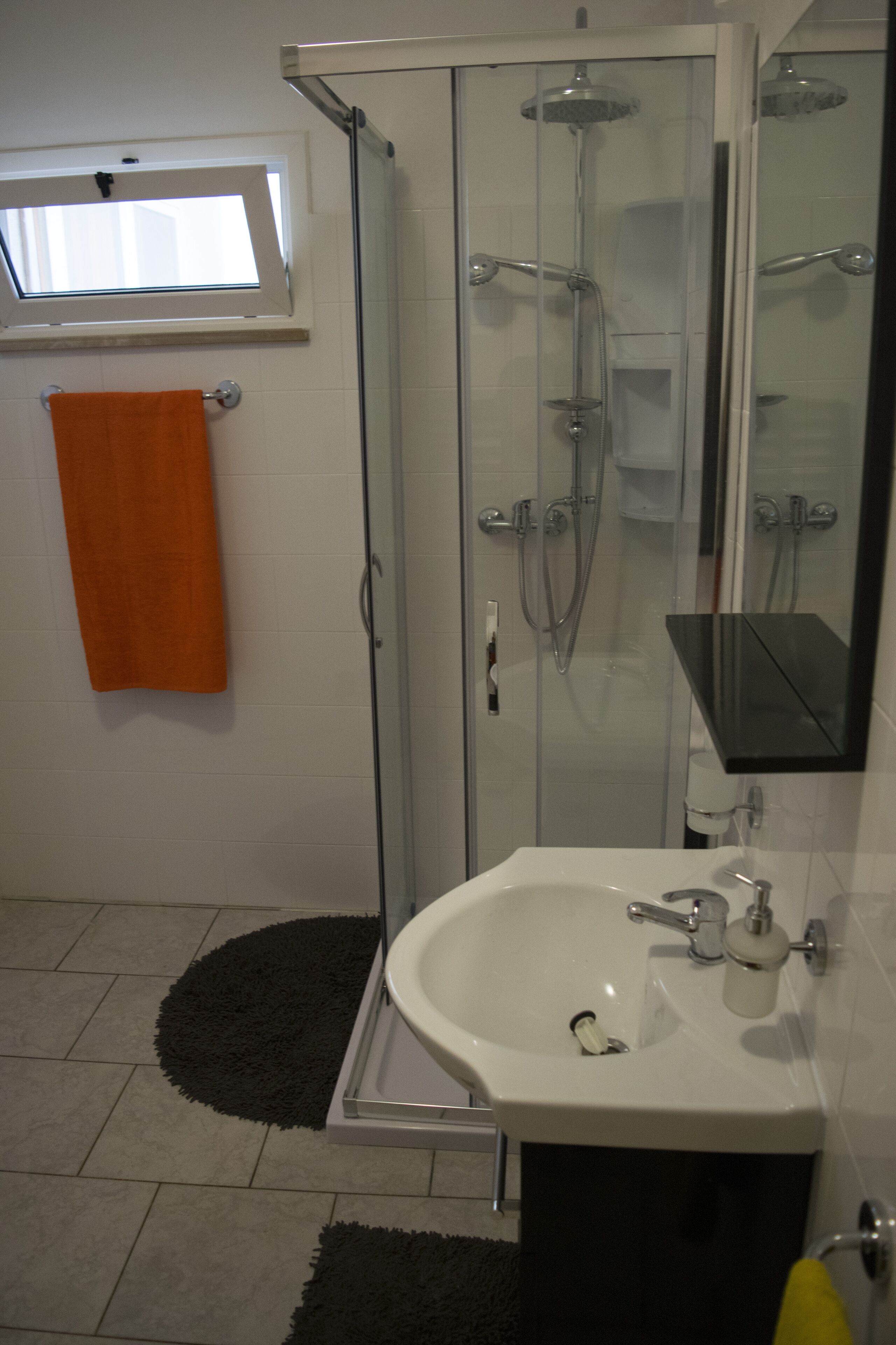 A modern bathroom with a glass-enclosed shower, a white sink, and a black rug.