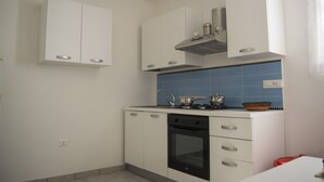 Eine kleine Küche mit weißen Schränken, einem schwarzen Backofen und einer blau gefliesten Spritzschutzleiste.