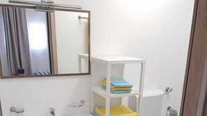 Ein Badezimmer mit Waschbecken, Spiegel und Toilette. Blaue und gelbe Handtücher liegen auf Regalen.