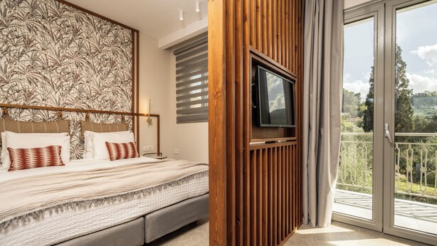 Un dormitorio con cama, televisor montado en un panel de madera y balcón con vistas.