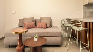 Un espacio habitable compacto con sofá, dos sillones, una mesita redonda y una zona de kitchenette.