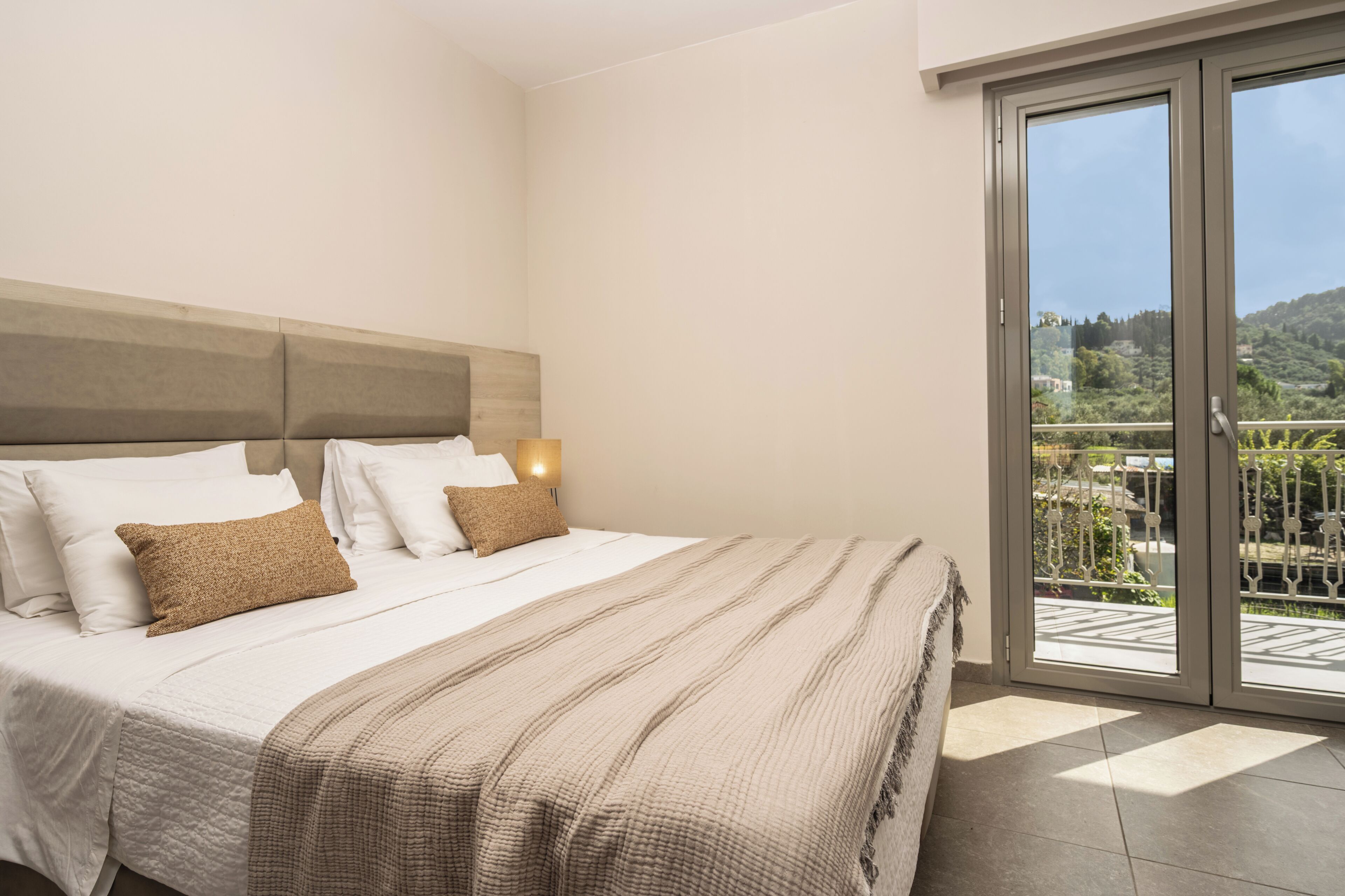 A bedroom with a bed, a nightstand, a window with a view of greenery, and a sliding glass door.