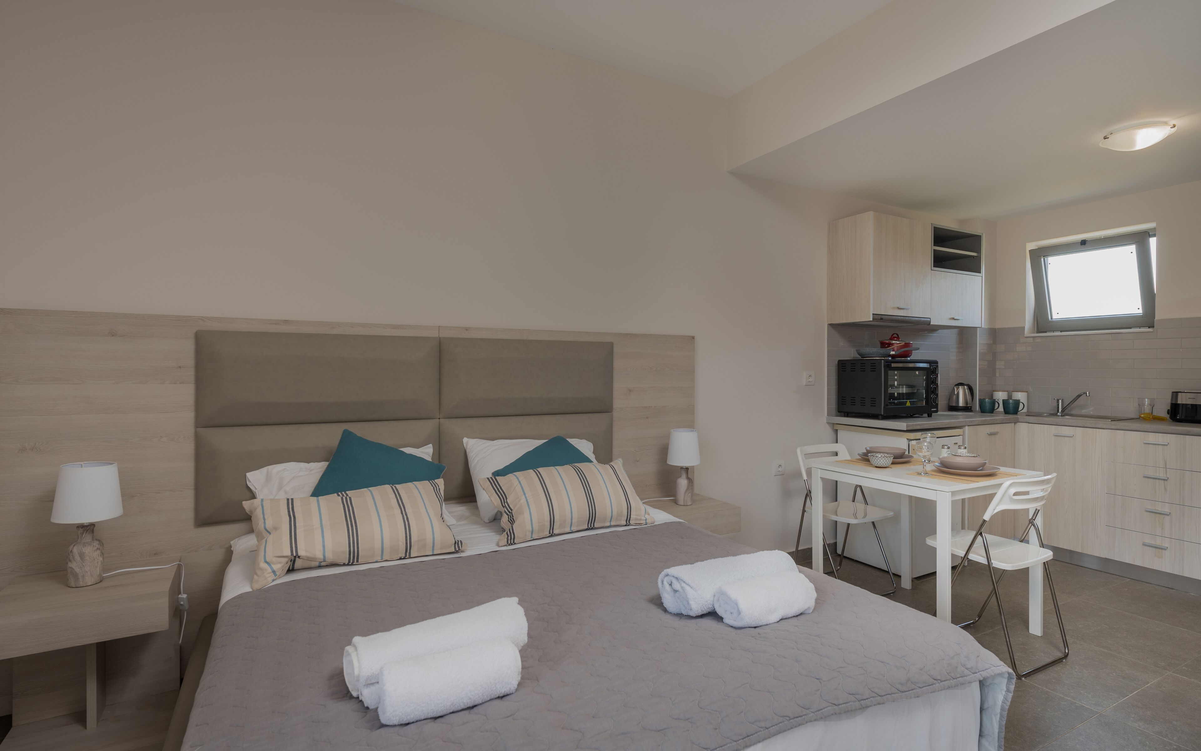 Un dormitorio con cama, mesitas de noche, una ventana y una kitchenette equipada con microondas, tostadora y lavabo.