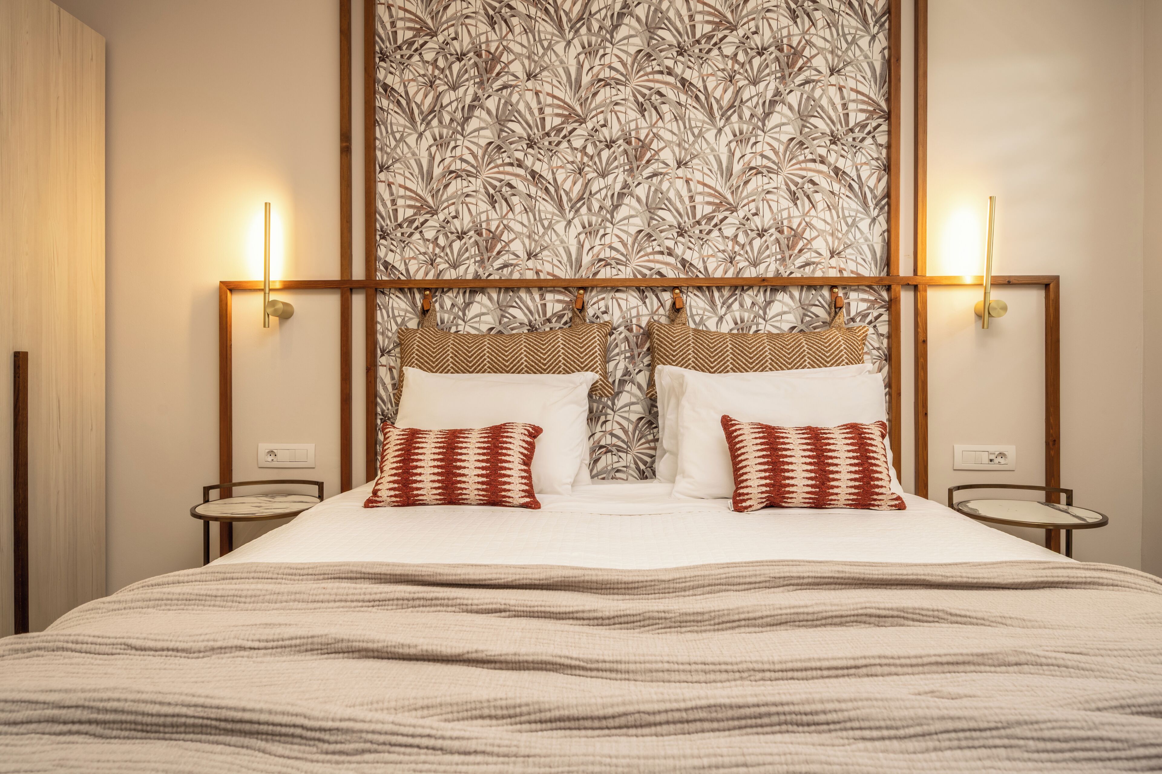 Hotelkamer met een groot bed, twee nachtkastjes, een muur met bladmotief en twee wandlampen.