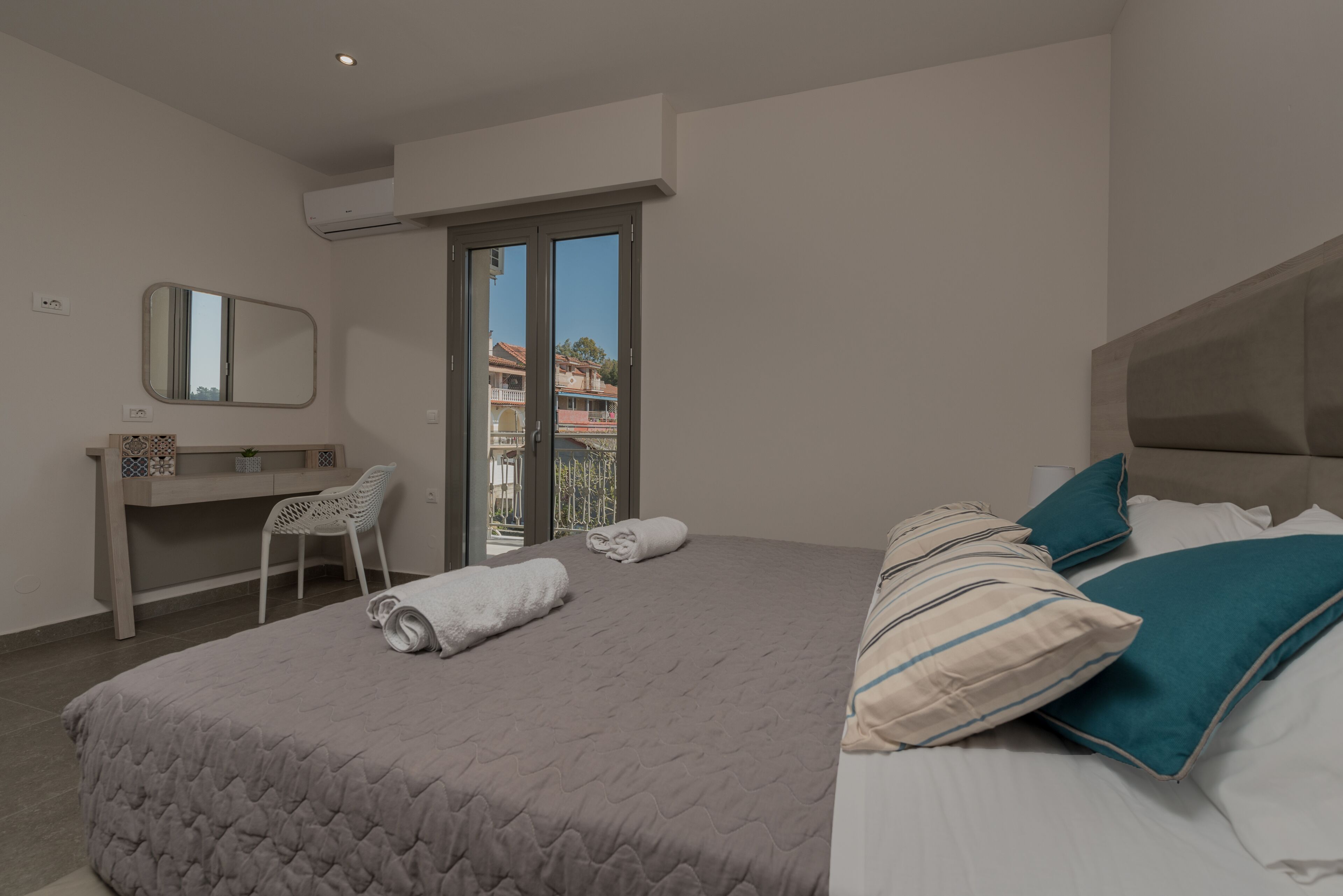 A bedroom with a bed, a desk, a chair, a window, and a balcony.
