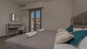 A bedroom with a bed, a desk, a chair, a window, and a balcony.