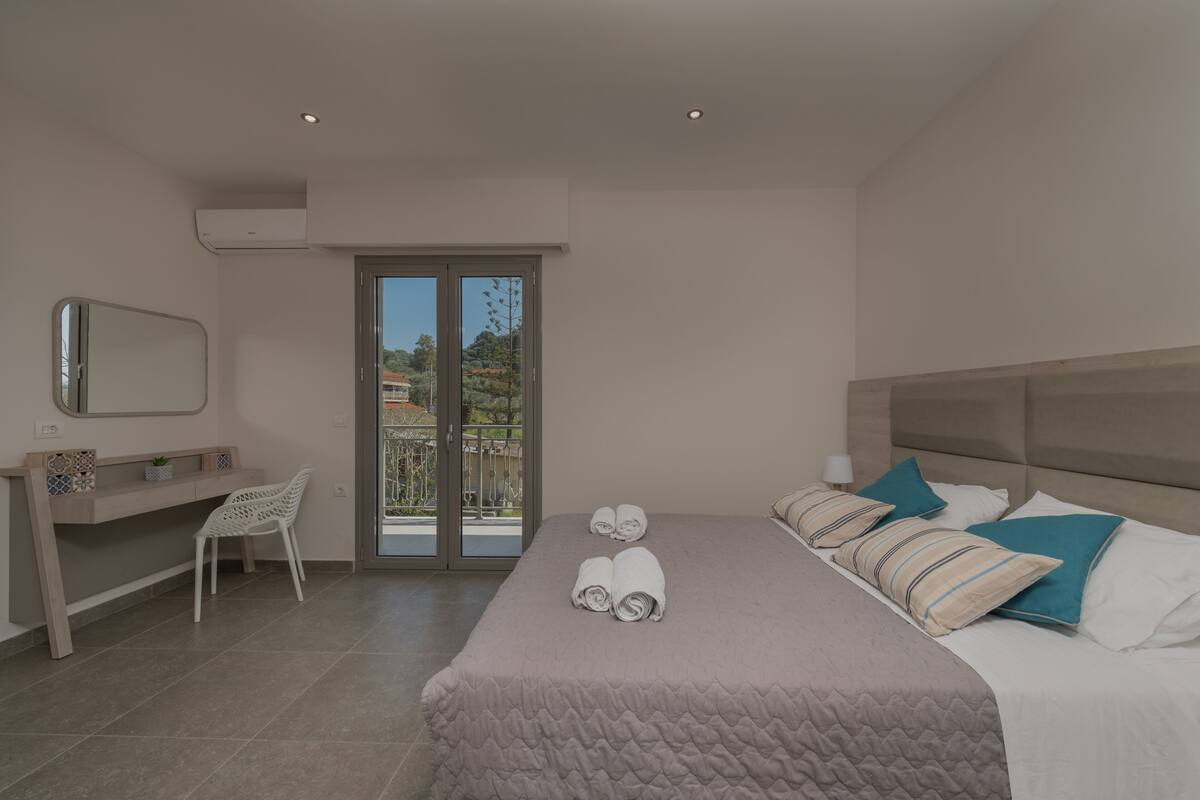 Habitación de hotel moderna con una cama grande, un escritorio, una silla y un balcón con vista a la ciudad.