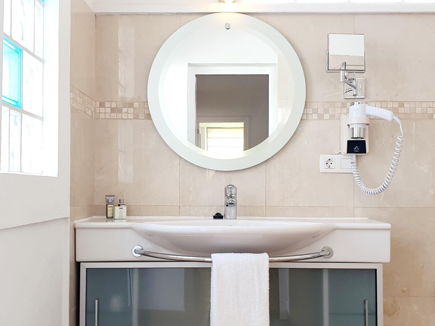 Une salle de bain avec un miroir rond, un lavabo et un porte-serviettes.