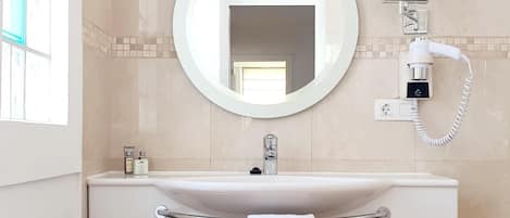 Une salle de bain avec un miroir rond, un lavabo et un porte-serviettes.