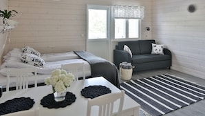 A room with a bed, a sofa, a dining table with a vase of flowers, and a window with curtains. - Valkeisen Loma (Ahtari)