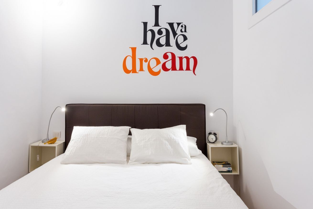 A neatly made bed with white bedding, a dark headboard, and a wall decal that reads "I have a dream".