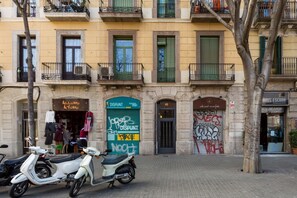 Un edificio con un negozio chiuso, una porta verde con graffiti e un albero di fronte.