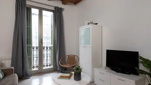 Un salon avec un canapé, une table basse ronde ornée de livres et d’une plante, un téléviseur posé sur un meuble, et un balcon avec vue.