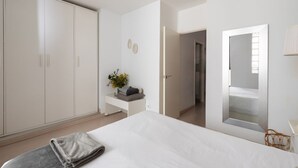 Une chambre à coucher avec un grand lit, une armoire, une table de chevet ornée d’un vase et un miroir au mur.