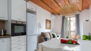 Une cuisine moderne avec des armoires blanches, un four encastré et un réfrigérateur blanc. On y trouve une table à manger avec des chaises et un luminaire suspendu en osier.