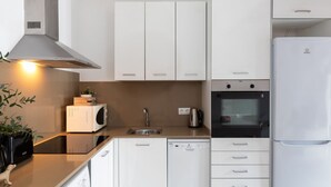 Une cuisine moderne avec des meubles blancs, un four encastré, un lave-vaisselle et un four à micro-ondes.