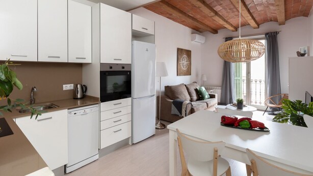 Une cuisine moderne avec des armoires blanches, un four encastré et un lave-vaisselle. On y trouve un coin repas avec une table et des chaises blanches, et un luminaire suspendu au-dessus.