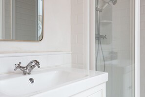 A bathroom with a white sink, a chrome faucet, and a glass-enclosed shower area. - Casa Cosi - Eixample 1 (Barcelona)