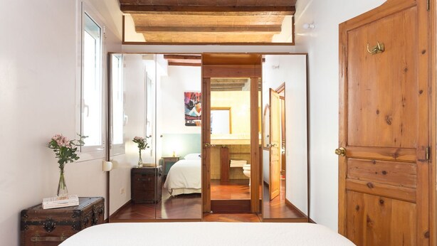 A bedroom with a wooden door, a bed, a suitcase, and a mirror. - Casa Cosi - Mallorca 1 (Barcelona)