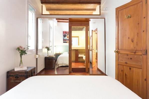 Une chambre avec une porte en bois, un lit, une valise et un miroir.