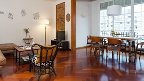 A living room with a sofa, a dining table with chairs, a TV, and a lamp. - Casa Cosi - Mallorca 1 (Barcelona)