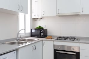Een moderne keuken met witte kasten, een ingebouwde magnetron, een broodrooster, een gasfornuis en een vaatwasser.