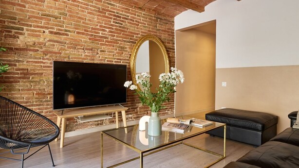 Un salon avec un mur en briques, un téléviseur à écran plat, un canapé, une table basse et un fauteuil.