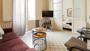 Una sala de estar acogedora con un sofá, una mesa redonda con limones, un televisor montado en la pared y una cama con vistas al exterior.