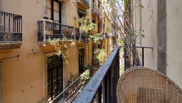 Una calle estrecha en la ciudad, con balcones, algunos con plantas y una bandera.