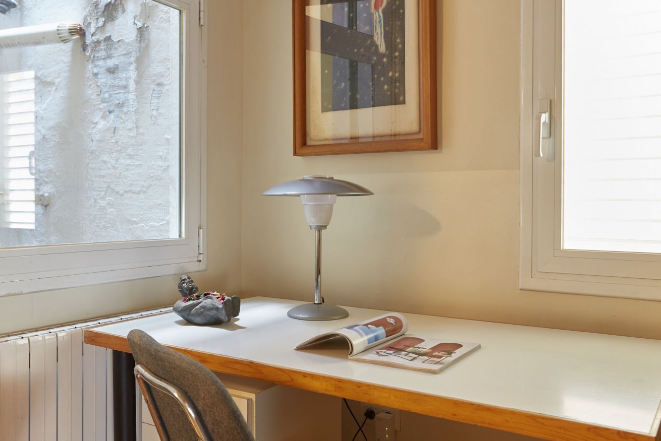 A room with a wooden desk, a lamp, a framed picture, and a window.