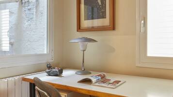 A room with a wooden desk, a lamp, a framed picture, and a window.