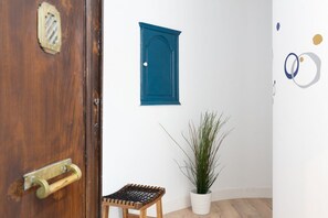 A wooden door with a brass handle, a blue-framed window, a small wooden stool, and a potted plant. - Casa Cosi - Eixample 2 (Barcelona)