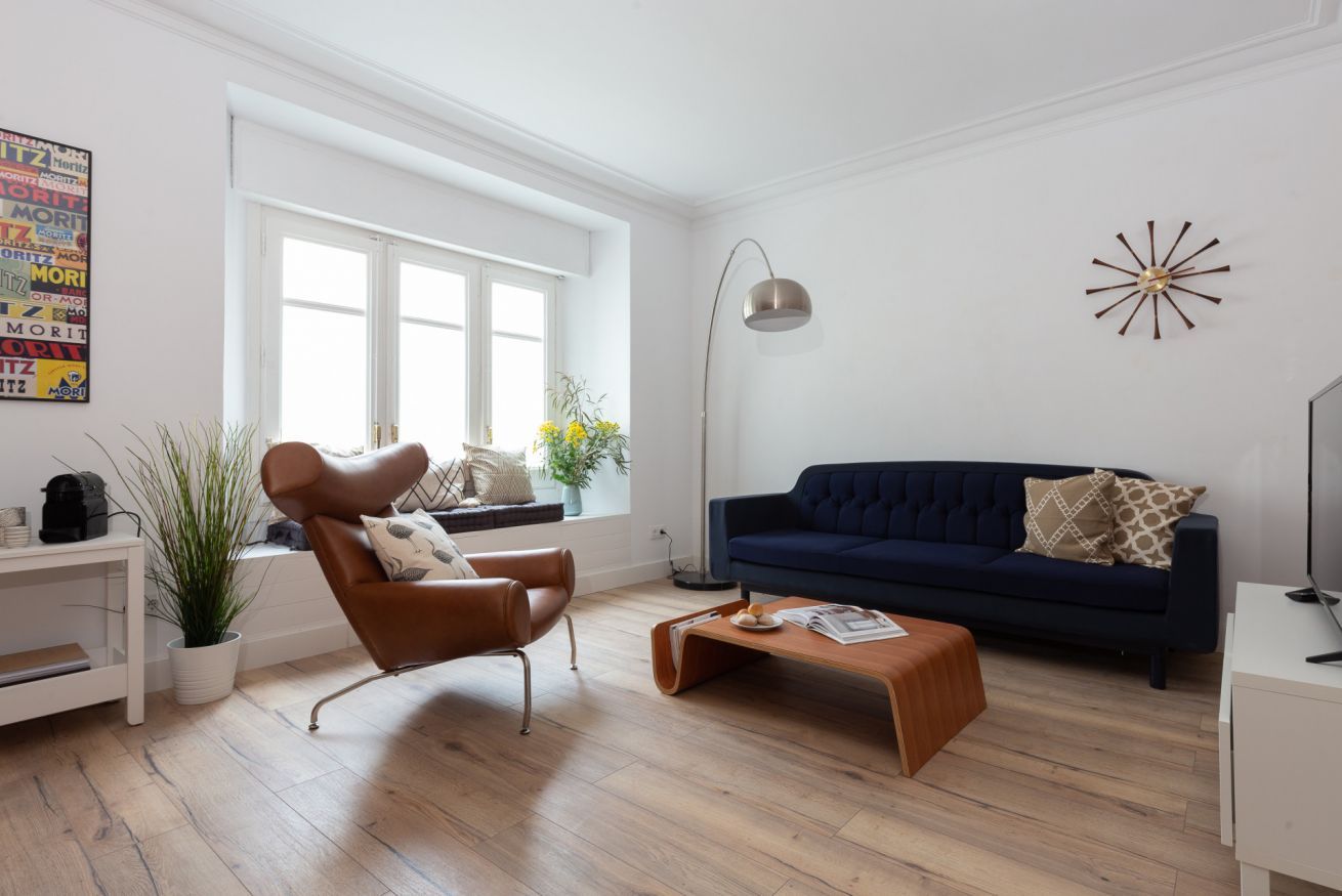 Una sala de estar moderna con un sofá azul oscuro, un sillón de cuero marrón, una mesa de centro de madera y una lámpara de pie.