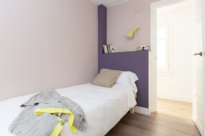 A bedroom with a single bed, a bedside table, a lamp, and a door. - Casa Cosi - Eixample 2 (Barcelona)