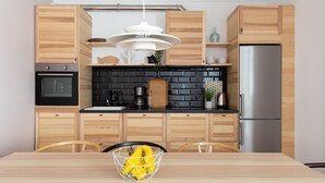 A modern kitchen with wooden cabinets, a black backsplash, stainless steel appliances, and a dining table with a fruit bowl. - Casa Cosi - Eixample 2 (Barcelona)